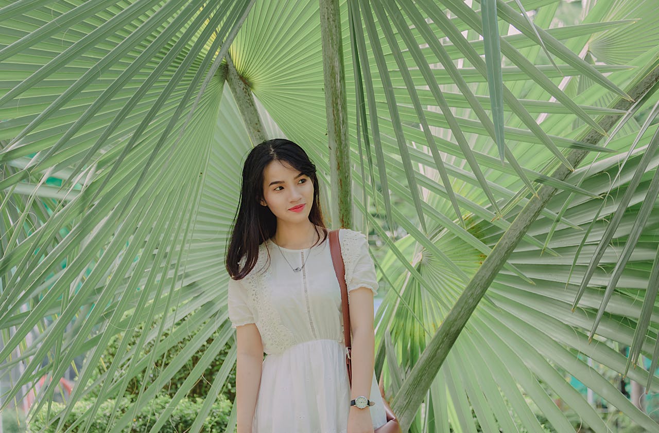 A young woman standing amidst tropical green palm leaves, exuding elegance and tranquility.